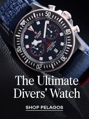 A close-up of a Tudor Pelagos chronograph watch with a blue dial, black bezel, and red accents, on a dark blue textile strap