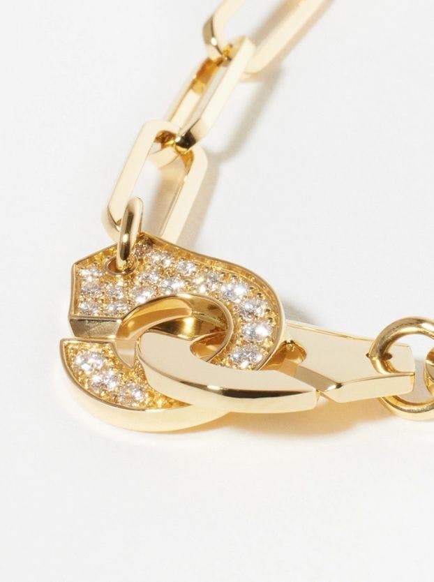 A close-up of a Dinh Van gold chain link necklace, focusing on its clasp which features two interlocking, curved "handcuff" shapes, one of which is entirely pavé-set with diamonds.