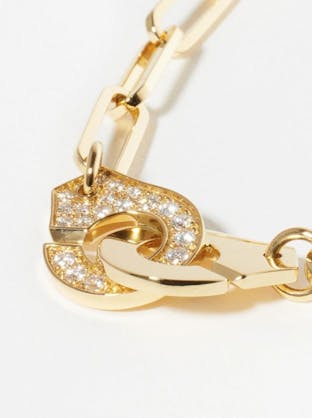 A close-up of a Dinh Van gold chain link necklace, focusing on its clasp which features two interlocking, curved "handcuff" shapes, one of which is entirely pavé-set with diamonds.