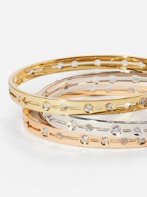 Three Dinh Van bangles are stacked, made of yellow gold, white gold, and rose gold. Each bangle has cut-out circular patterns interspersed with small, bezel-set diamonds.