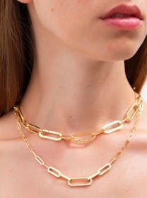 A close-up of a woman's neck and chest showcasing two layered gold Dinh Van chain necklaces with elongated, rectangular links; the lower necklace features one link entirely pavé-set with diamonds.