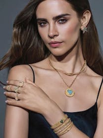 The jewelry includes textured gold pieces: a heart pendant necklace with a blue stone, a pearl ring, bangles with a green stone, and a star earring, all from the Future Fortune collection.