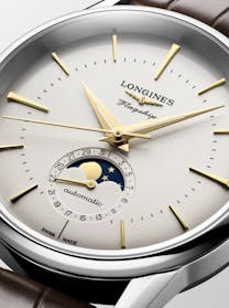 A close-up of a Longines Flagship watch dial, showing gold hands and markers, a moon phase complication, and a date sub-dial.