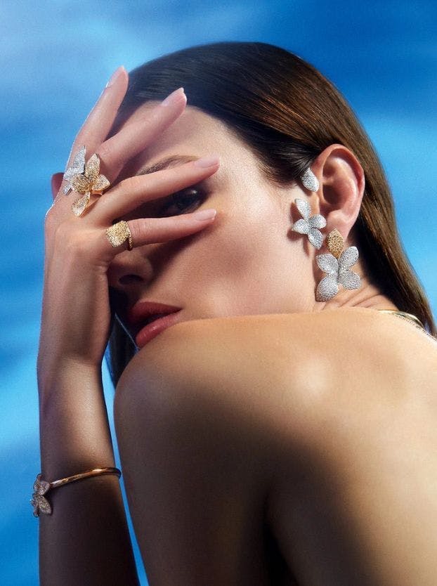 A woman with brown hair poses, adorned in diamond-encrusted floral earrings, a matching flower ring, and a diamond bracelet.