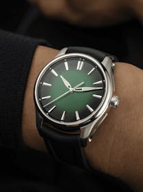 A close-up of a man's wrist wearing an H. Moser & Cie. Pioneer watch with a vibrant green fume dial and a black rubber strap, available at The 1916 Company.