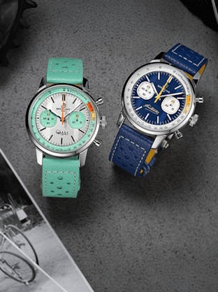 A pair of Breitling Top Time Coppi collection watches, one with a light green dial and strap and the other with a dark blue and yellow strap, available at The 1916 Company.
