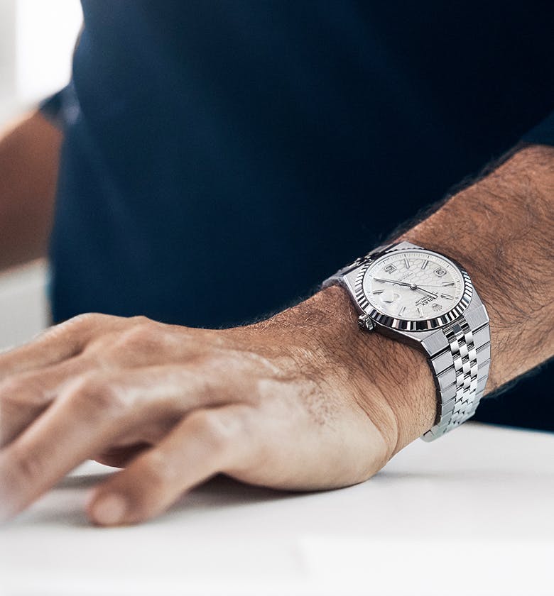 A shot of the wrist of a man wearing a silver Rolex Land-Dweller