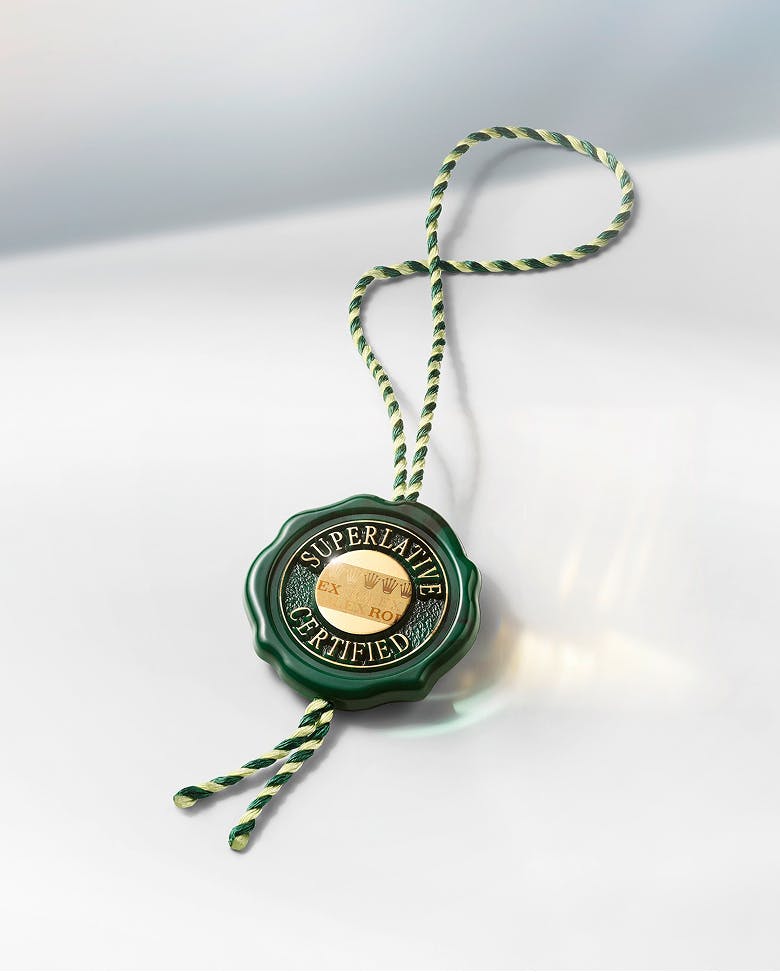 A close-up of the Rolex Superlative Certified Seal, featuring a green and gold medallion with an intricate braided cord, symbolizing the brand's commitment to excellence.