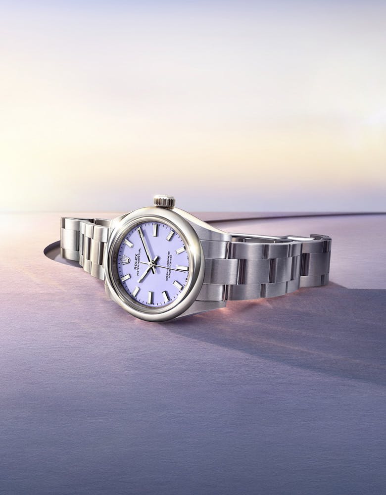 Rolex Oyster Perpetual with silver bracelet and purple dial laying on a gradient purple surface