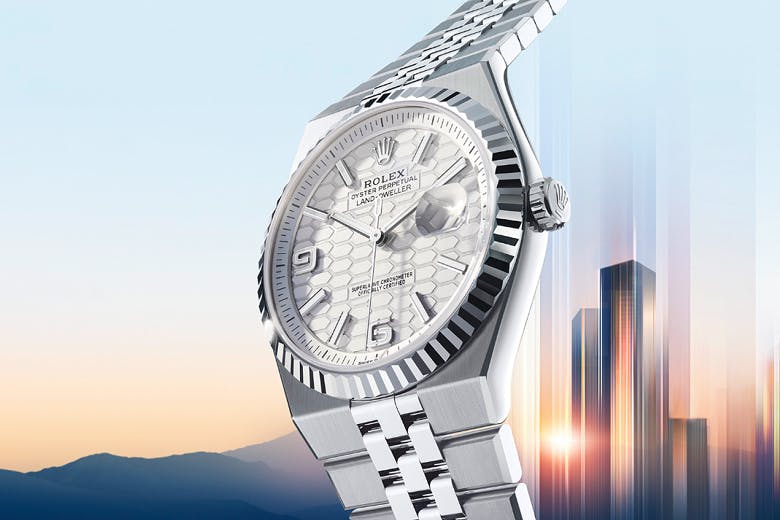 Rolex Land Dweller in silver with a fluted bezel, shown against a glowing skyline and mountain horizon.