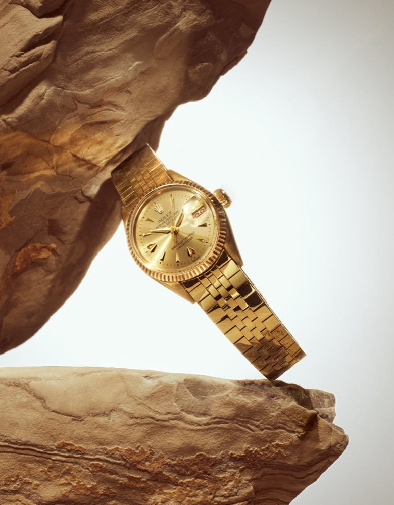 A Rolex Lady Datejust watch with a gold bracelet is artfully positioned between two rocks, showcasing its refined elegance and classic design.
