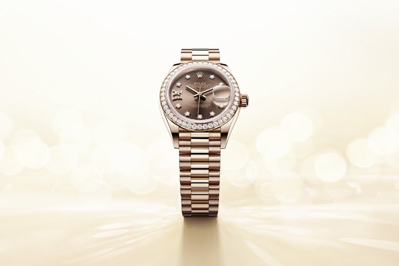 Rolex Lady Datejust watch with a diamond bezel, champagne dial, and gold bracelet displayed on an elegant, light background