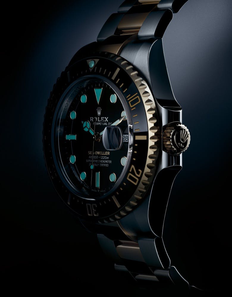 A side view of a Rolex Sea Dweller watch with a black dial and luminescent markers, featuring a two-tone gold and silver bezel, set against a dark background.