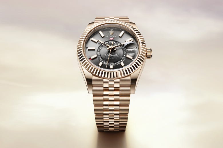 A Rolex Sky-Dweller watch with a silver dial and a gold bracelet, displayed against a softly lit, gradient background.