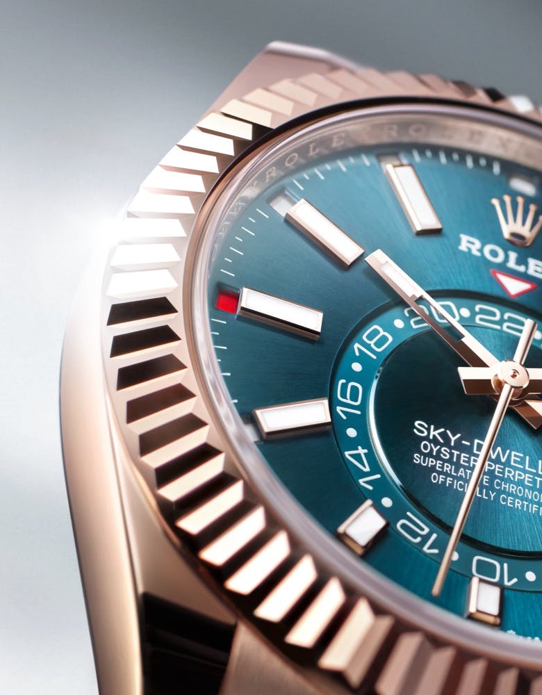 A close-up of a Rolex Sky-Dweller watch with a blue dial and a gold bezel, displayed against a softly lit background.