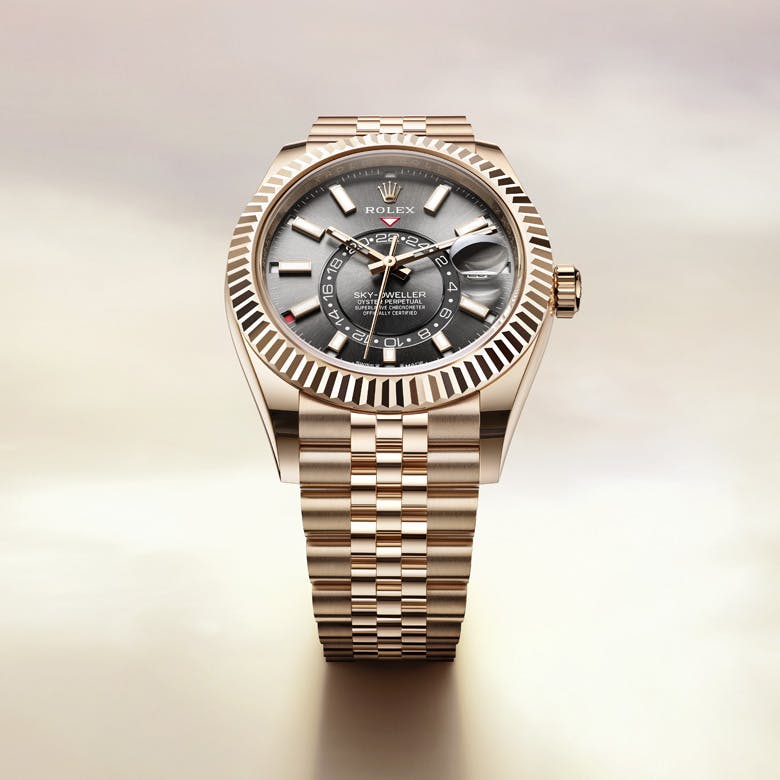 A Rolex Sky-Dweller watch with a silver dial and gold bracelet, displayed against a soft, light background.