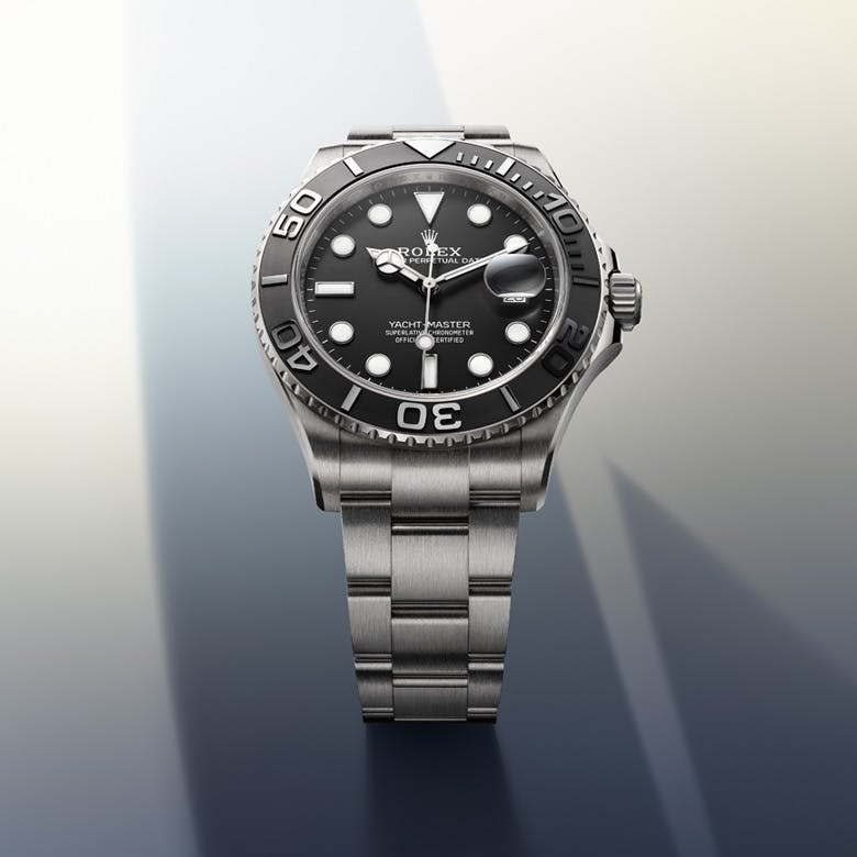 A Rolex Yacht-Master watch with a black dial and silver bracelet, displayed against a gradient background.