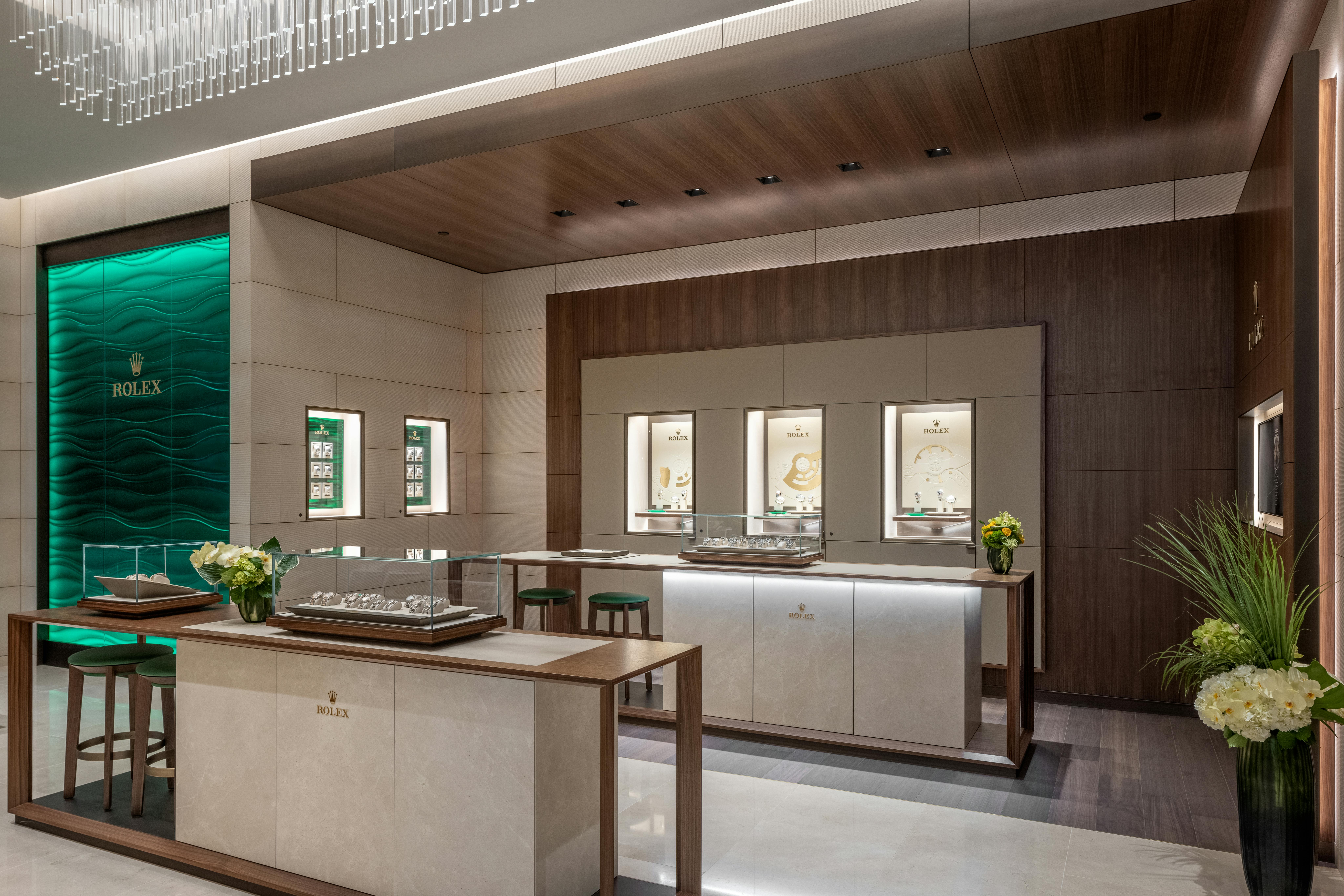 A modern Rolex showroom with elegant display counters, green and wood accents, and illuminated showcases on the walls.