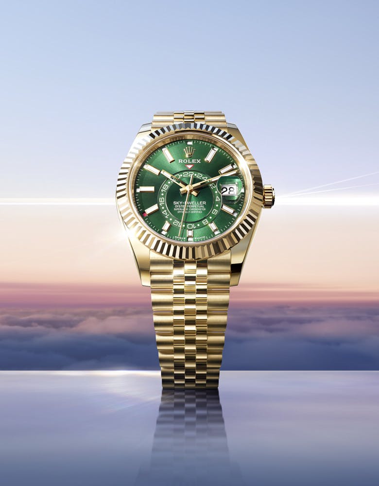 A Rolex Sky-Dweller watch with a green dial, gold bezel, and gold bracelet, displayed against a cloudy sky background with soft lighting.